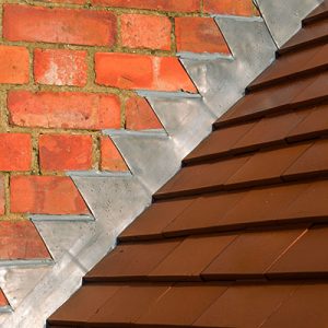 Closeup of new plain red clay tiles and lead flashing on a pitched roof in the UK.